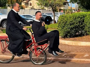 De bike e megafone, padres viram comédia convidando para a novena